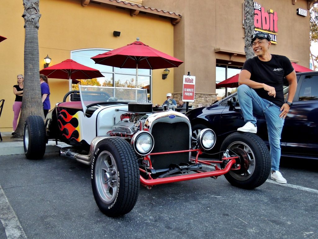 Ed posing proudly with a classic hot rod featuring flame graphics in front of The Habit Burger Grill in Simi Valley.